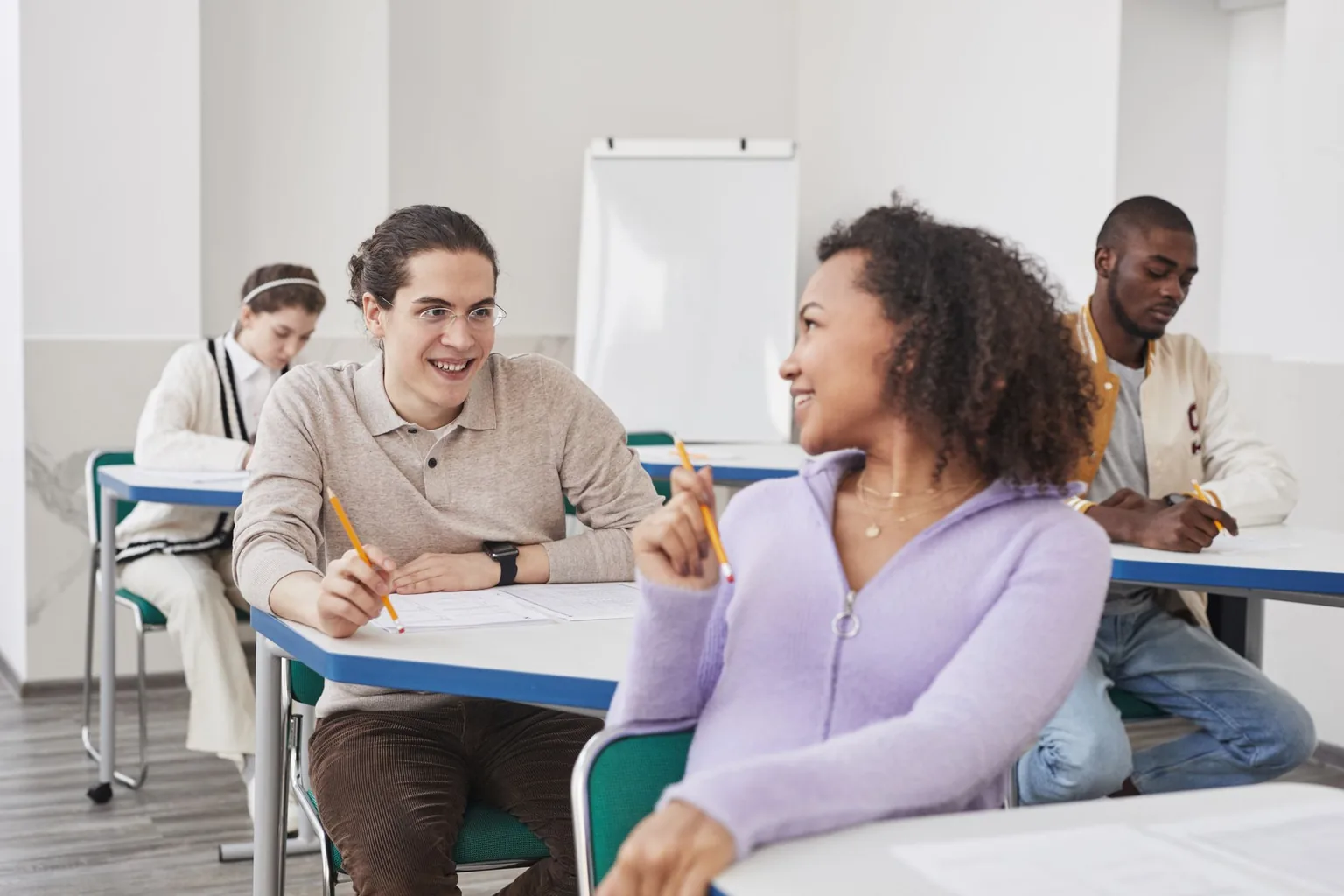 Adult learners talking and laughing in pairs in a bright English classroom